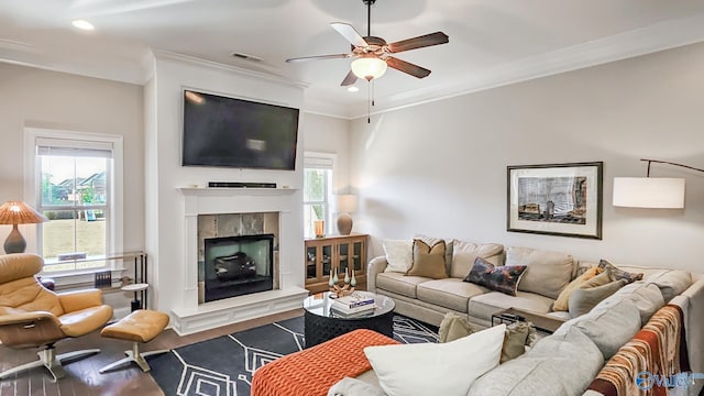 living room featuring visible vents, a ceiling fan, a tiled fireplace, wood finished floors, and crown molding