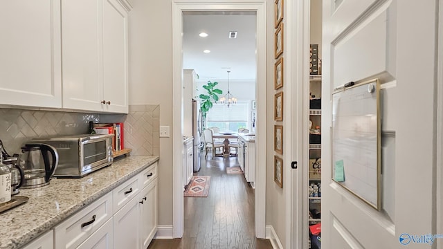 kitchen with white cabinetry, decorative backsplash, light stone countertops, a chandelier, and dark wood-style flooring