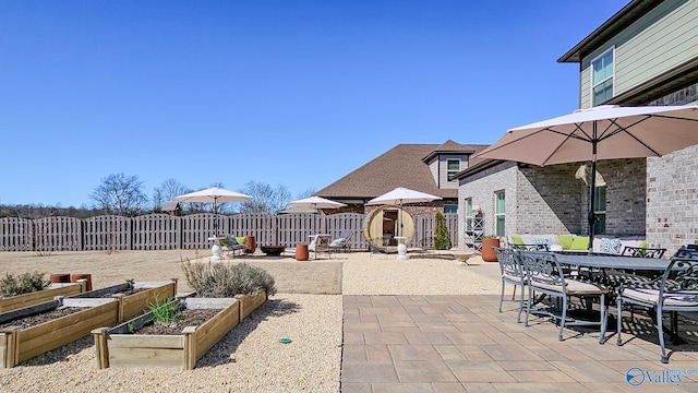 view of patio with outdoor dining area, a vegetable garden, and fence