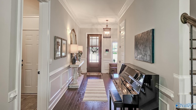 foyer featuring a notable chandelier, dark wood finished floors, a decorative wall, wainscoting, and crown molding