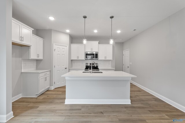 kitchen with appliances with stainless steel finishes, light hardwood / wood-style floors, hanging light fixtures, and an island with sink