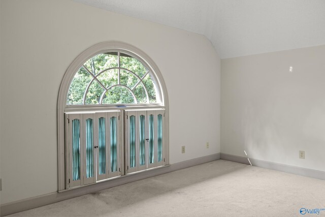 carpeted spare room with vaulted ceiling