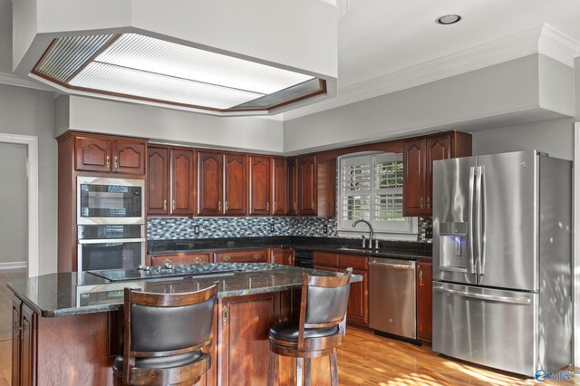 kitchen with a center island, appliances with stainless steel finishes, dark stone counters, and light hardwood / wood-style floors