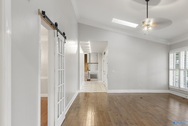 interior space with light wood-type flooring, crown molding, ceiling fan, and a barn door