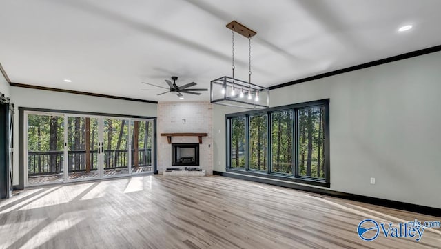 unfurnished living room with a fireplace, light wood-type flooring, ceiling fan with notable chandelier, brick wall, and ornamental molding