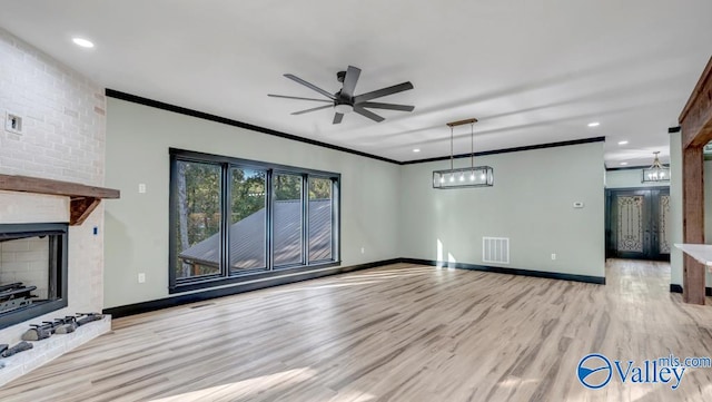 unfurnished living room with a fireplace, ceiling fan, crown molding, light wood-type flooring, and brick wall