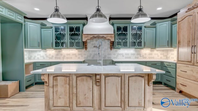 kitchen featuring decorative light fixtures, decorative backsplash, sink, a center island with sink, and light hardwood / wood-style floors