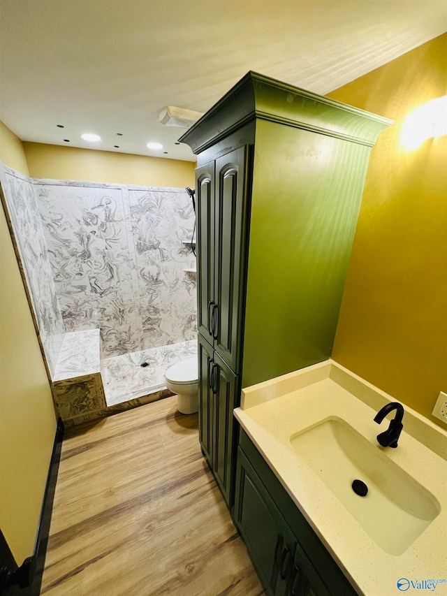 bathroom featuring tiled shower, vanity, wood-type flooring, and toilet