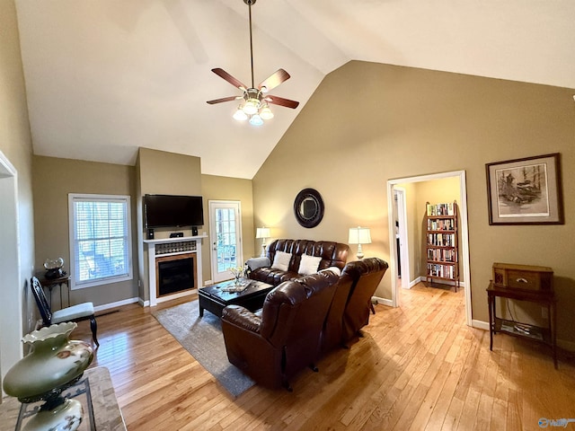 living area featuring a ceiling fan, baseboards, high vaulted ceiling, a fireplace, and light wood-style floors