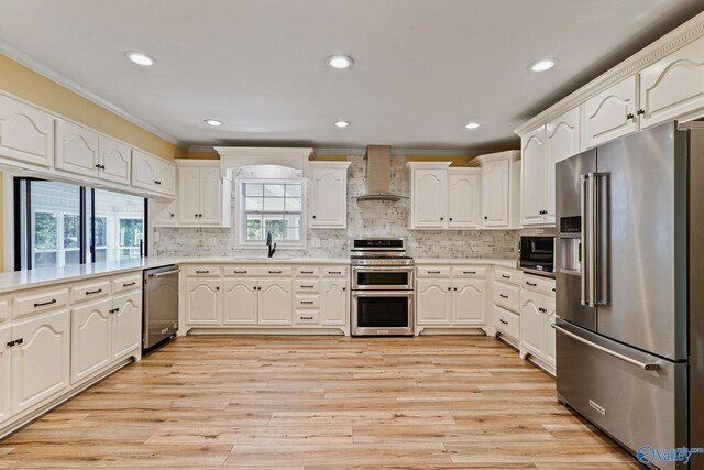 kitchen featuring high end appliances, wall chimney exhaust hood, light wood-type flooring, and backsplash