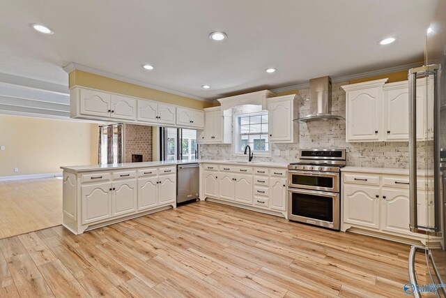 kitchen featuring appliances with stainless steel finishes, decorative backsplash, light hardwood / wood-style floors, kitchen peninsula, and wall chimney range hood