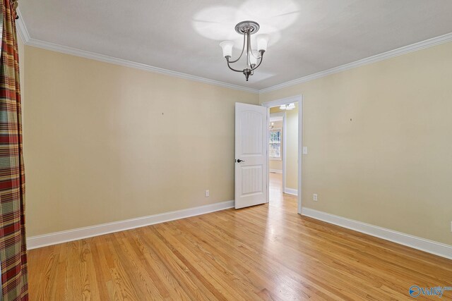 empty room featuring crown molding, light hardwood / wood-style floors, and a chandelier