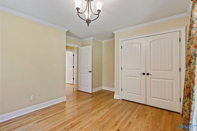 unfurnished bedroom featuring crown molding, light hardwood / wood-style flooring, a closet, and a chandelier