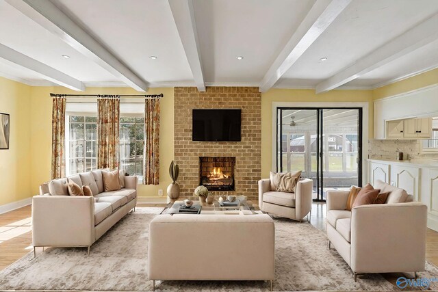 living room with a fireplace, beam ceiling, light hardwood / wood-style floors, and a healthy amount of sunlight