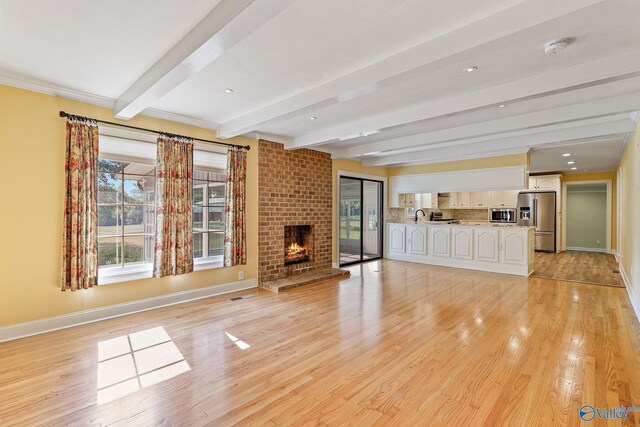 unfurnished living room featuring a fireplace, beamed ceiling, light hardwood / wood-style flooring, and brick wall