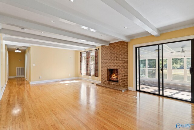 unfurnished living room with ceiling fan, a fireplace, beamed ceiling, and light wood-type flooring