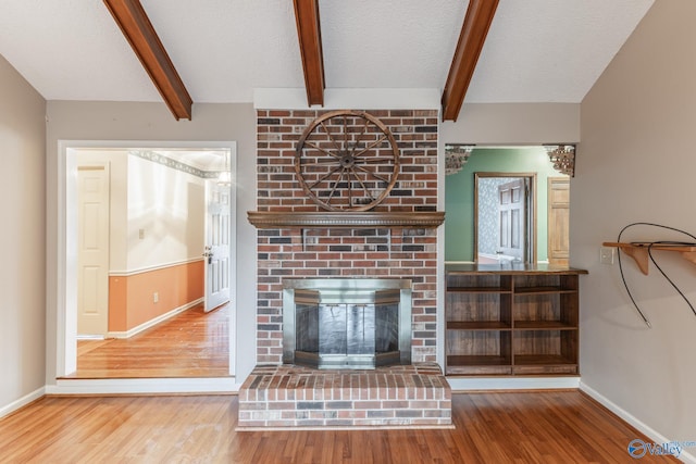 unfurnished living room featuring wood finished floors, baseboards, beam ceiling, a fireplace, and a textured ceiling