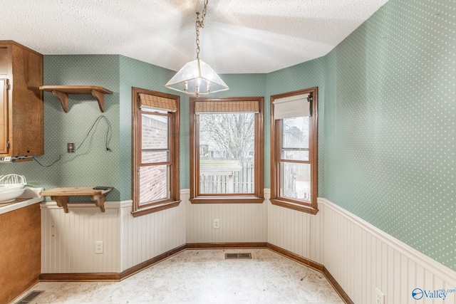 unfurnished dining area with visible vents, wainscoting, a textured ceiling, and wallpapered walls