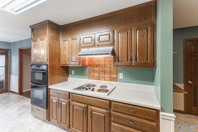 kitchen featuring wallpapered walls, under cabinet range hood, light countertops, electric stovetop, and dobule oven black