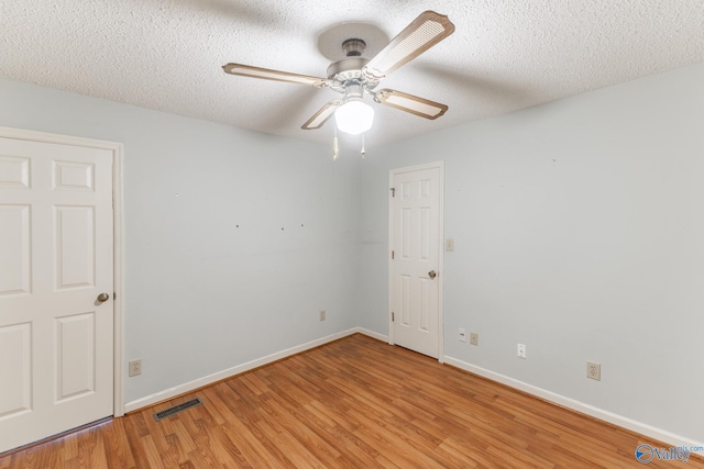 empty room featuring a ceiling fan, baseboards, visible vents, a textured ceiling, and light wood-type flooring