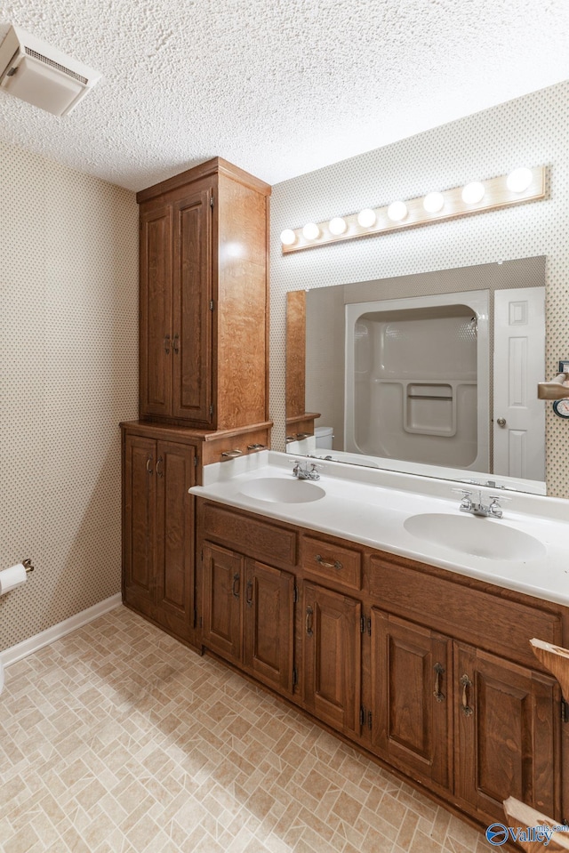 bathroom featuring visible vents, a textured ceiling, wallpapered walls, and a sink