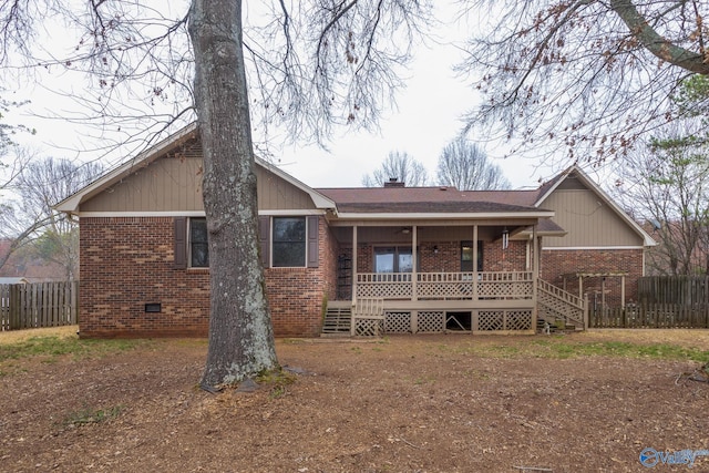 back of house featuring brick siding, a porch, a chimney, and fence