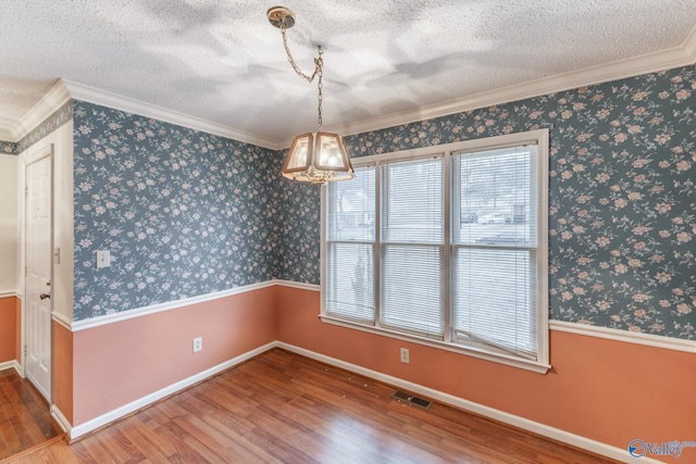 unfurnished dining area with wallpapered walls, wood finished floors, visible vents, and a textured ceiling