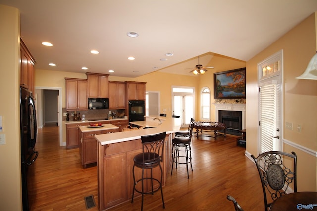 kitchen featuring a kitchen bar, tasteful backsplash, dark hardwood / wood-style floors, a kitchen island with sink, and black appliances