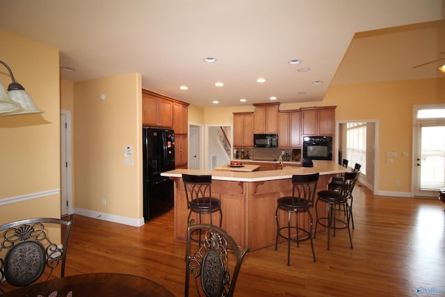 kitchen featuring a kitchen bar, wood-type flooring, black appliances, and a center island with sink