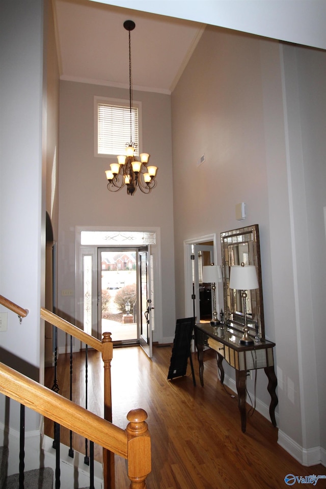 entryway featuring hardwood / wood-style flooring, a towering ceiling, ornamental molding, and an inviting chandelier