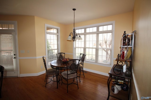 dining area with dark wood-type flooring, plenty of natural light, and an inviting chandelier