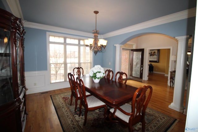 dining space with wood-type flooring, ornamental molding, a chandelier, and ornate columns