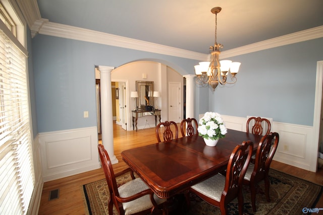 dining space featuring ornamental molding, wood-type flooring, a chandelier, and decorative columns