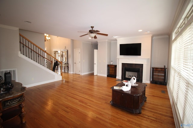 living room featuring a tiled fireplace, ceiling fan with notable chandelier, wood-type flooring, and ornamental molding