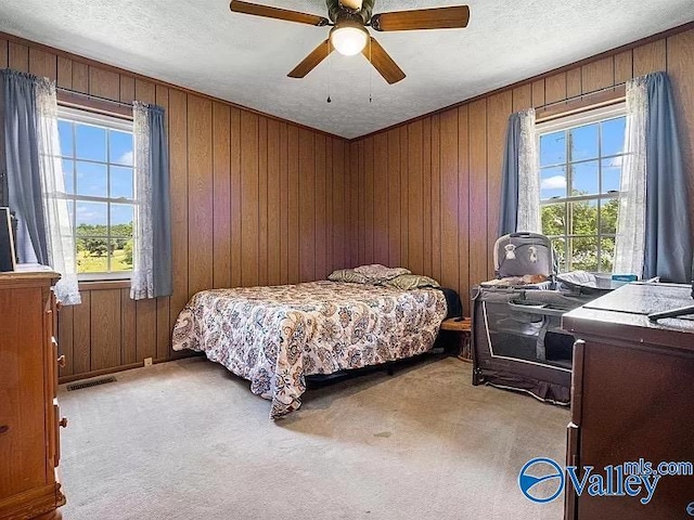 bedroom featuring light carpet, wooden walls, and a textured ceiling