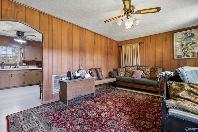 living room featuring ceiling fan, heating unit, a textured ceiling, and wood walls