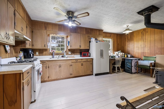 kitchen featuring sink, wood walls, white appliances, light hardwood / wood-style flooring, and ceiling fan