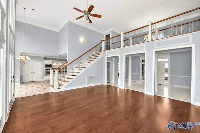 unfurnished living room with hardwood / wood-style floors, ceiling fan with notable chandelier, a high ceiling, and ornamental molding