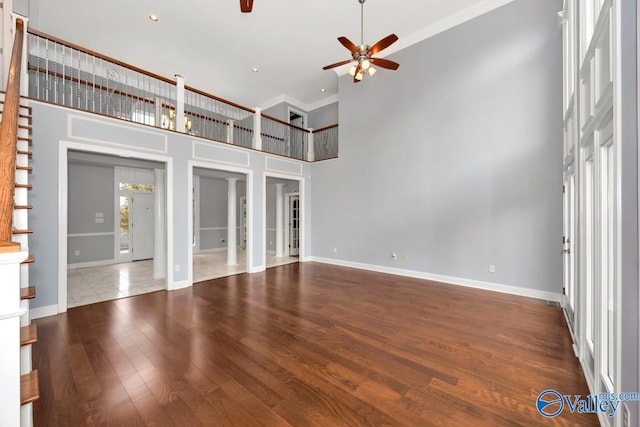 unfurnished living room with ceiling fan, wood-type flooring, a high ceiling, and ornamental molding