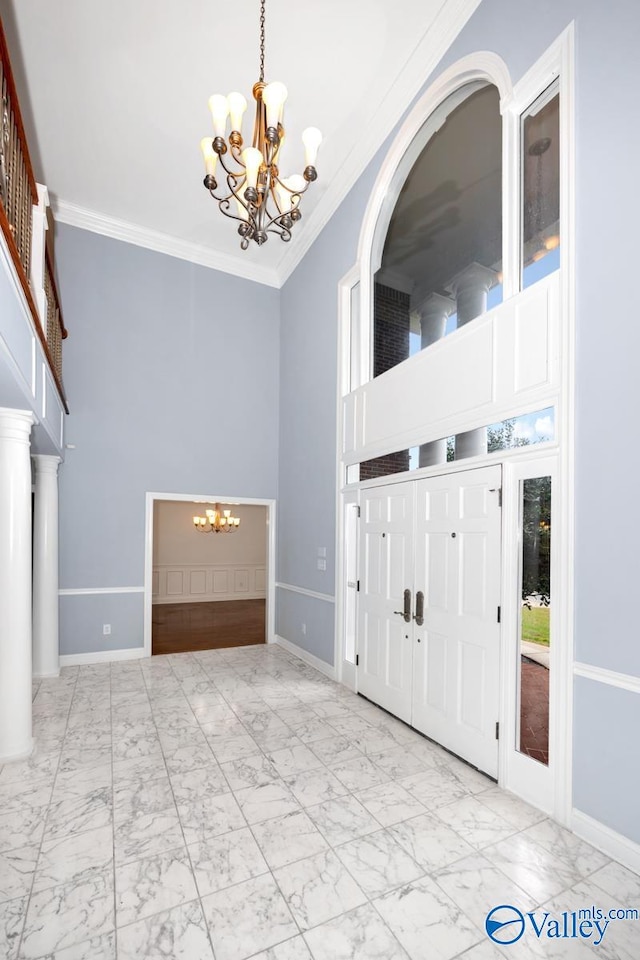 foyer with decorative columns, crown molding, a towering ceiling, and a notable chandelier