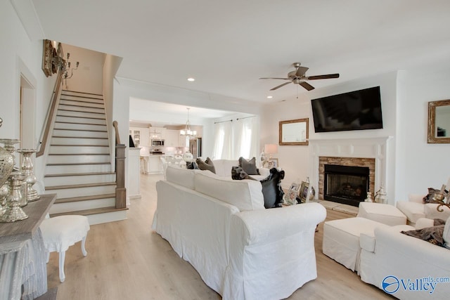 living room with a fireplace, recessed lighting, stairway, light wood-type flooring, and ceiling fan with notable chandelier