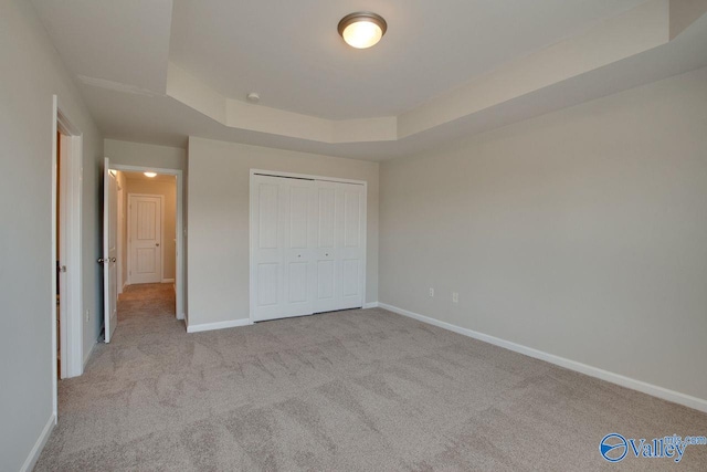 unfurnished bedroom featuring a raised ceiling, light colored carpet, and a closet