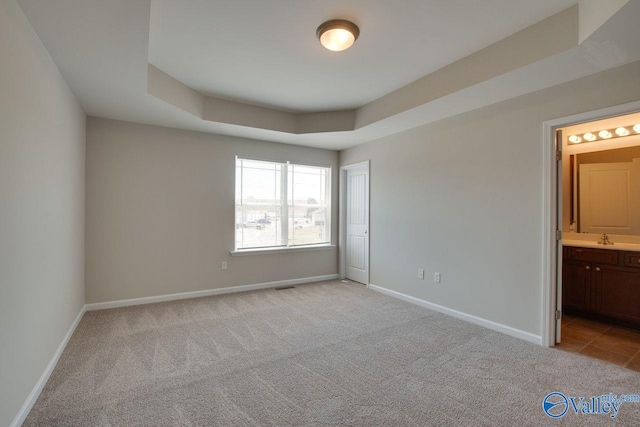 unfurnished bedroom featuring ensuite bathroom, sink, light carpet, and a raised ceiling