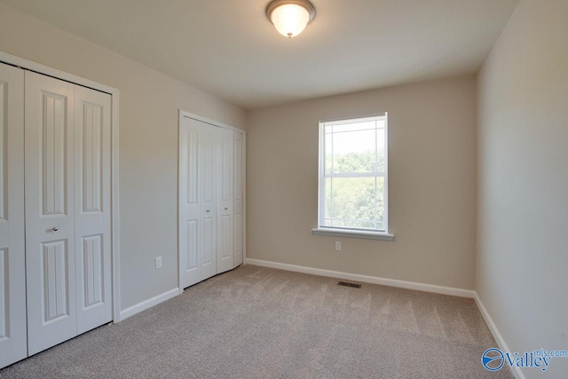 unfurnished bedroom featuring two closets and light carpet