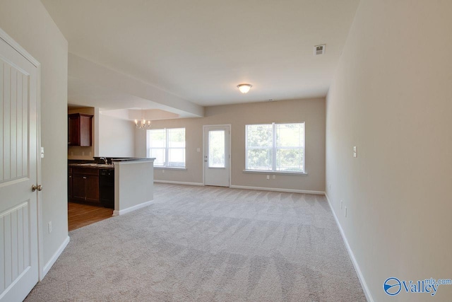 unfurnished living room with sink, light carpet, and a notable chandelier