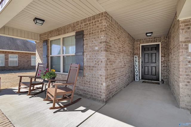 view of exterior entry featuring brick siding and covered porch