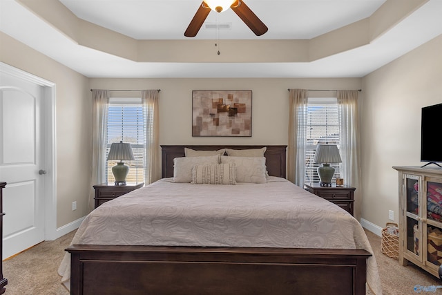 bedroom with a raised ceiling, baseboards, visible vents, and light carpet