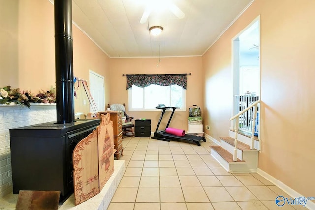 workout area with light tile patterned floors, crown molding, ceiling fan, and a wood stove