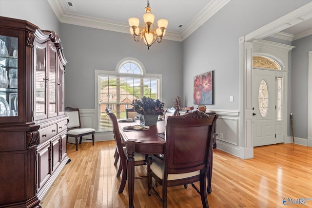 dining room with light wood-style flooring, a chandelier, crown molding, and wainscoting