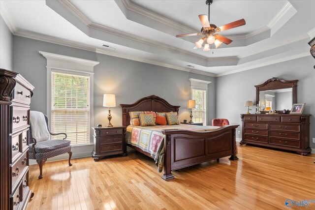 bedroom featuring a raised ceiling, crown molding, multiple windows, and light wood-type flooring